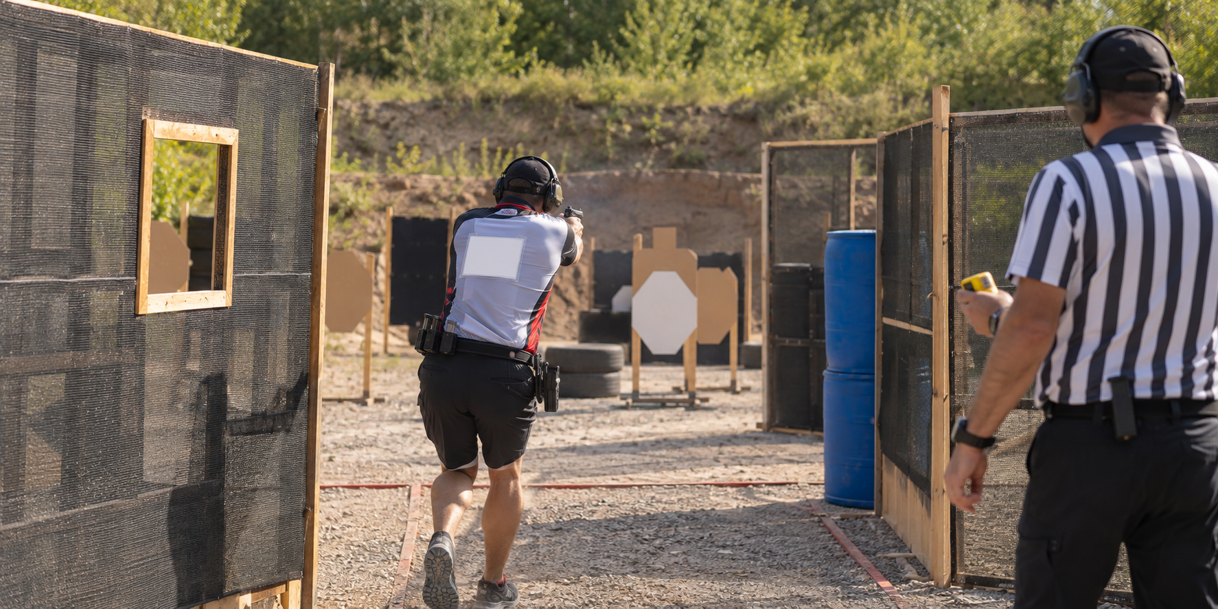Erwachsener Teilnehmer und Aufsicht bei einem IPSC-Wettkampf auf einem Schießstand, von hinten gesehen